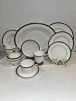 Front view of various pieces including plates, cups, saucers, and a covered sugar bowl showing white china with black and gold trim.