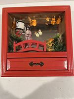 Front view of red wooden jewelry box with glass-fronted diorama featuring geisha, butterfly, flowers, and red bridge.