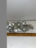 Front view of the crystal grape cluster showing the faceted grape spheres and attached glass leaves laid flat next to a ruler for size reference.