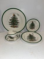 Photo of the Spode Christmas Tree dinnerware set showing the four pieces: dinner plate, bread plate, soup bowl, and tea cup with saucer, all decorated with the Christmas Tree design and green rim.