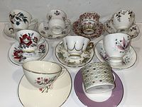 Top view of 8 tea cup and saucer sets showing varied floral designs and color patterns including reds, blues, pinks, and gold accents.