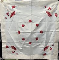 Full view of square table cover showing embroidered strawberry needlework design scattered across the center and corners with a textured border.