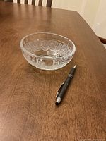 Photo showing one small clear crystal bowl with a textured circular pattern, next to a pen for scale reference.