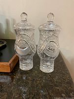 Pair of clear crystal lidded vases with detailed cut patterns on dark granite surface