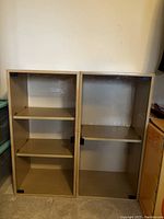 Two small light brown wooden bookcases or shelves with no glass doors, each with two shelves inside.