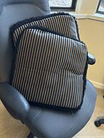 Two square throw pillows with beige and black stripes and black fringe trim on edges, placed on a gray chair.