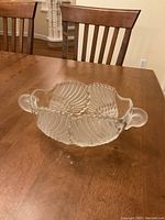 Clear crystal bowl with ribbed ribbed shell pattern and two handles, shown on wooden dining table.