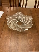Photo showing a flat crystal bowl with an artistic swirl pattern and a central hole, placed on wooden dining table.