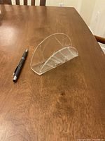 Clear glass napkin holder placed on wooden table next to a pen for scale.