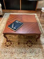Top view of square mahogany coffee table with Britannia album and remote controls on top to show scale and surface detail
