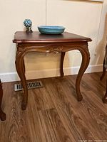Side view of a mahogany side table showing carved floral detailing and curved legs on hardwood floor.