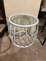 Circular white metal side table with vertical bars and clear glass top, showing some scuffing on the metal frame.