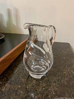 Photo showing a small clear crystal jug with etched swirl patterns, a curved handle, and a pouring spout.