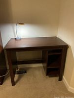 Small brown wooden desk with flat top, three shelves on right side, and a lamp on top (lamp not included). Small chipping visible on left front side of desk.