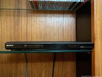 Front view of Sony black DVD player showing Sony logo, DVD and HDMI labels, placed on a wooden shelf.