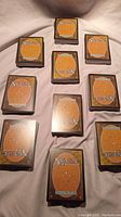 Ten stacks of Magic the Gathering cards arranged on a fabric surface showing the back design of the cards.