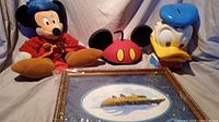 Photo showing the Fantasia Magician Sorcerer Mickey Mouse plush, the Donald Duck piggy bank, and the framed Disney Cruise Line pin together