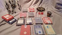 Lot displaying dice clock with black dice, assorted casino playing card decks, Sands ashtray, red dice, and shot glass on beige fabric background