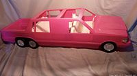 Side view of the pink plastic vintage Barbie limousine car showing six wheels including dual rear tires and open roof design.