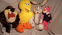Four vintage plush stuffed animals posed together: Tasmanian Devil, Big Bird, Bugs Bunny, Pink Panther.