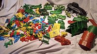 Lot of assorted vintage plastic toy soldiers in blue, red, yellow, green, with toy tanks and vehicles around.