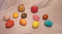 Collection of 9 colorful polished semi precious stone eggs and 2 polished stone apples arranged on fabric background.