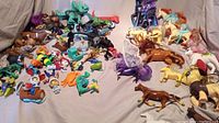 Large assortment of small toys including horses, dinosaurs, cartoon characters, and other small figurines spread out on a cloth.