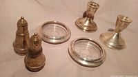 Photo showing the two sterling silver candlesticks, salt and pepper shakers, and ashtrays on a cloth background.