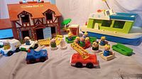 Photo of vintage Fisher Price Little People play house, boat, several vehicles, figures, and accessories arranged on a surface, showing the full lot.
