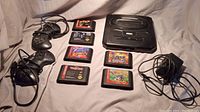 Photo showing Sega Genesis console with two wired controllers, nine game cartridges arranged in two rows, and power adapter.
