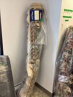 Rolled up wool area rug wrapped in plastic, label visible with size and brand.