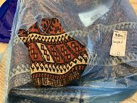 Area rug wrapped in blue plastic tarp, showing folded tribal geometric pattern with red, black, cream colors and MaxSold label.