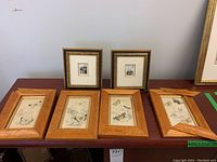 Six framed art prints on table: four butterfly prints in light wood frames and two cityscape prints in gold and black decorative frames.