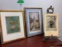 Shows three prints together, two framed in gold-tone frames, one unframed print on brass stand