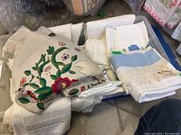 Photo showing assorted folded bed sheets, pillow cases, napkins, runners, and cloths with embroidery and lace edges.