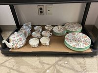 Full set view showing teapot, creamer, sugar bowl, cups, saucers, and stacked plates on a shelf.
