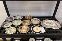 Ten round saucers and stack of rectangular plates on metal shelving