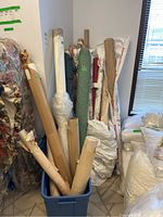 Multiple upright rolls of fabric and wallpaper in bin, various patterns and packaging