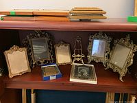 Overview of all eight frames arranged on a shelf, showing variety of decorative metal frames and some stacked wooden frames on top.