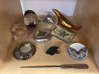 Overview of nine items including paperweights, metal figures, letter opener and coin cube