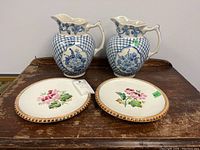 Two Ashworth plates and two blue and white ceramic pitchers on a wooden surface.