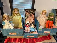 Front view of the seven dolls seated in three blue Madame Alexander boxes, showing various traditional and character costumes.