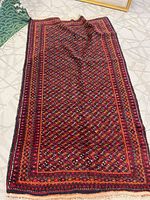 Full view of rectangular area rug on floor showing red geometric pattern and fringe.