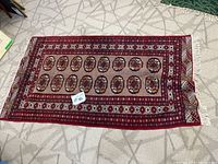 Full view of the red oriental style area rug laid flat on a light geometric area rug showing the full detailed pattern and fringed edges.