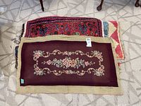 Top view of three stacked small area rugs showing two floral needlepoint and one red patterned rug.