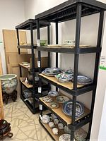 Two resin shelving units with black frames, each having four beige-colored shelves, shown with various ceramic and porcelain decorative items on shelves. Units measure approximately 35x17x74 inches.