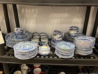 Three-tiered shelving with stacks of blue and white Spode Blue Italian plates, cups, mugs, sugar bowl and creamer