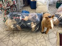 View of large bag with multiple assorted stuffed animals inside including black dog and tan animals, plus separate tan horse toy standing next to it
