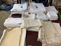 Wide view of assorted table linens stacked on table, mainly white fabric with some lace edges.