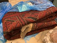 Folded red and black wool rug on blue plastic cover